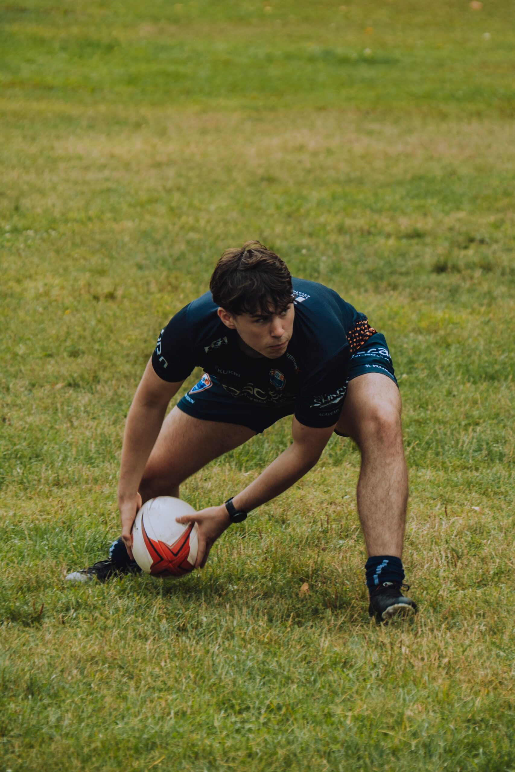 Teenage rugby player preparing for a pass during an outdoor match on a grassy field.